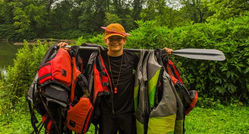 a student carries life jackets hanging on a paddle on a canoeing trip near DC